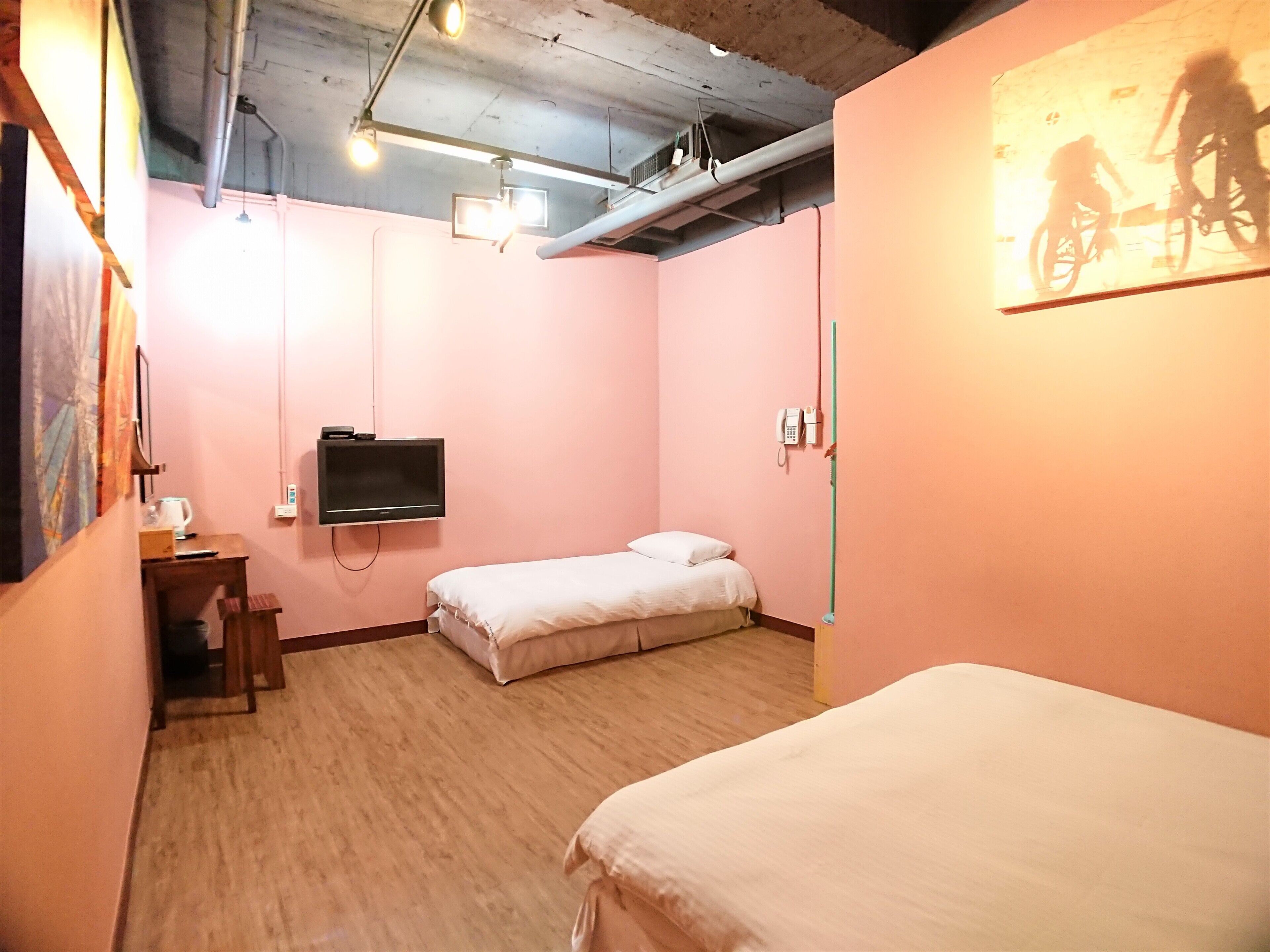 A room with two beds, a TV mounted on the wall, a phone, and a painting of cyclists.