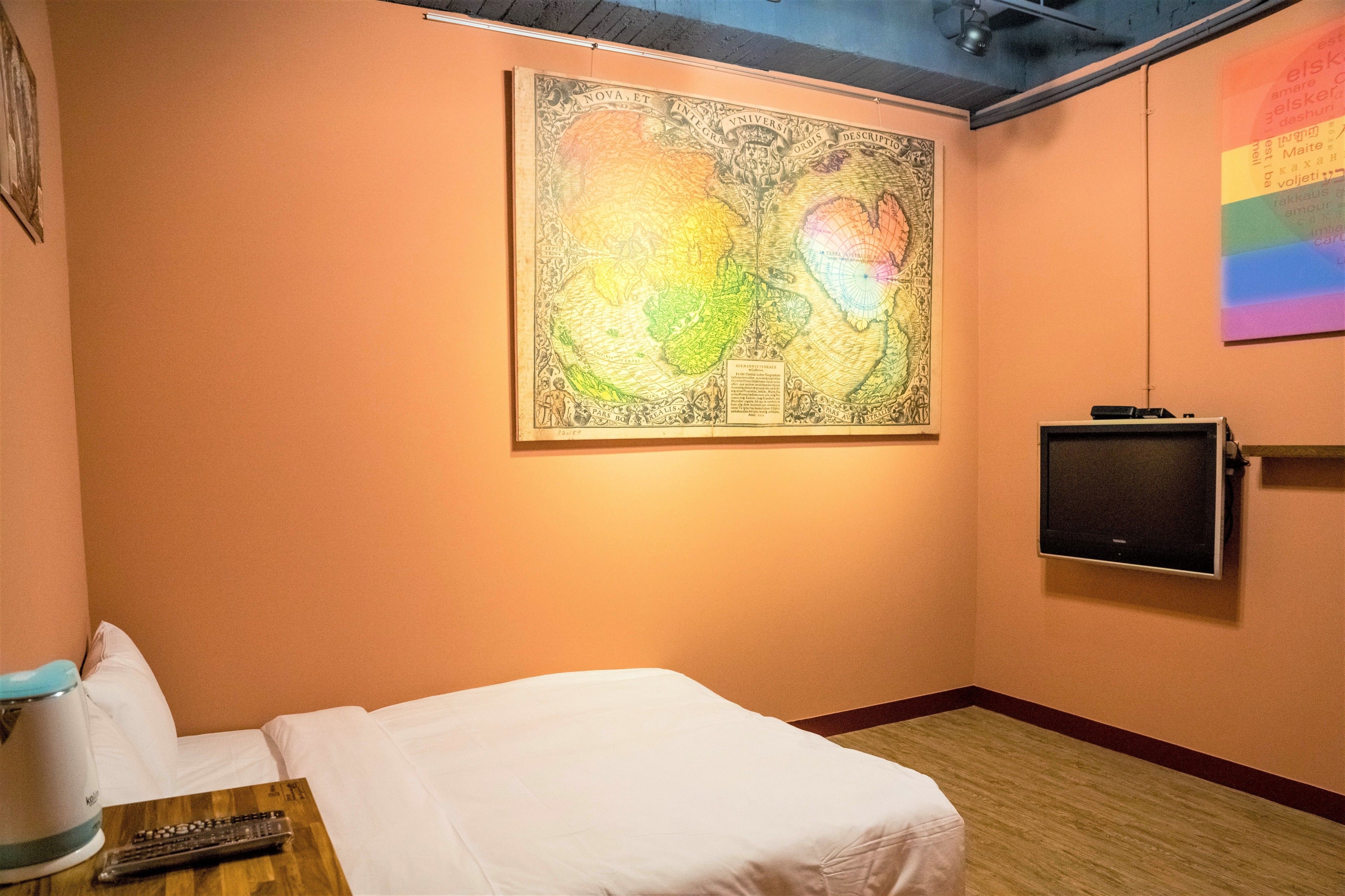 A hotel room with a bed, a television mounted on the wall, and a large map artwork above the bed.
