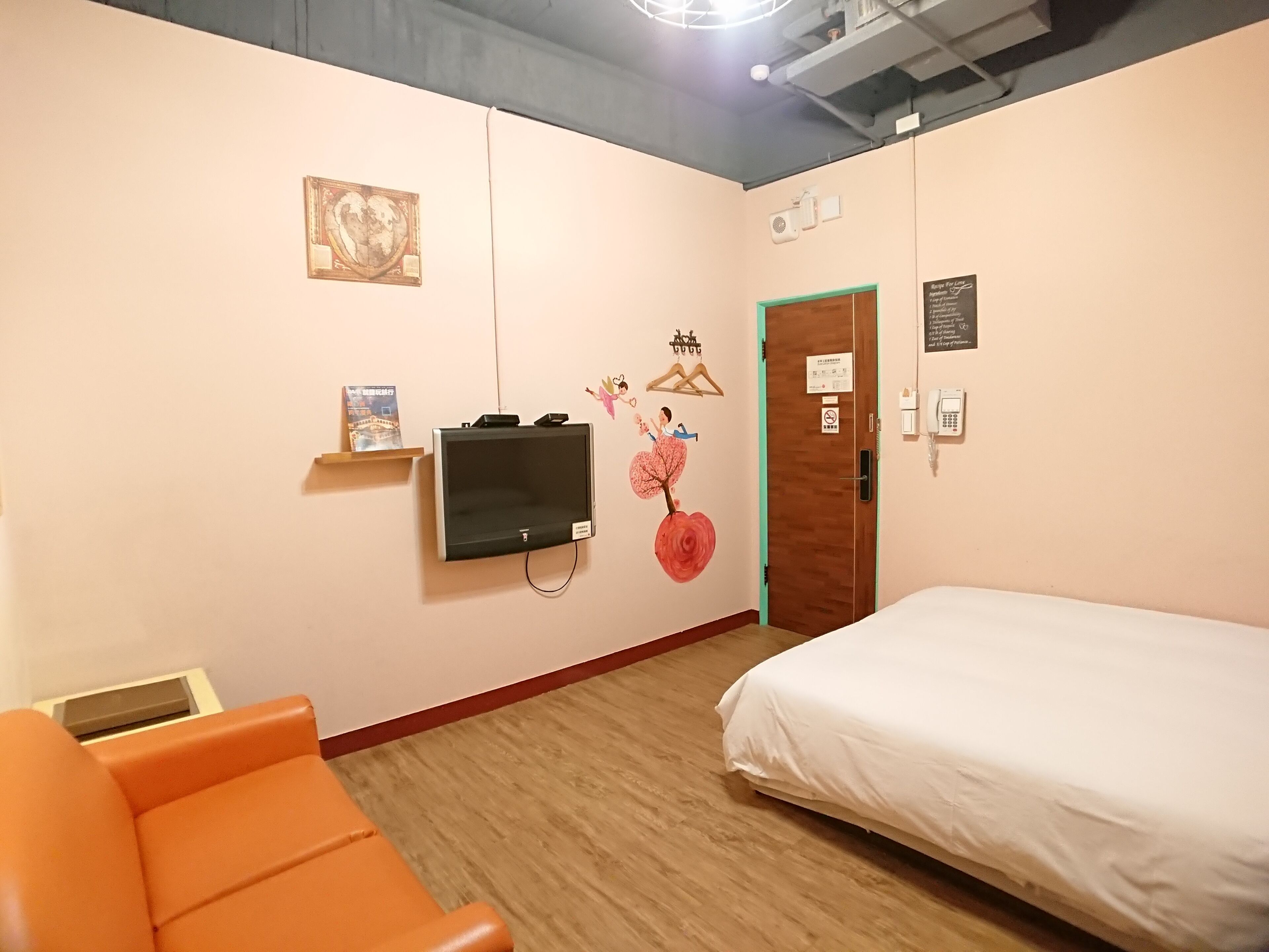 A hotel room with a bed, an orange chair, a television mounted on the wall, and a door with a green frame.
