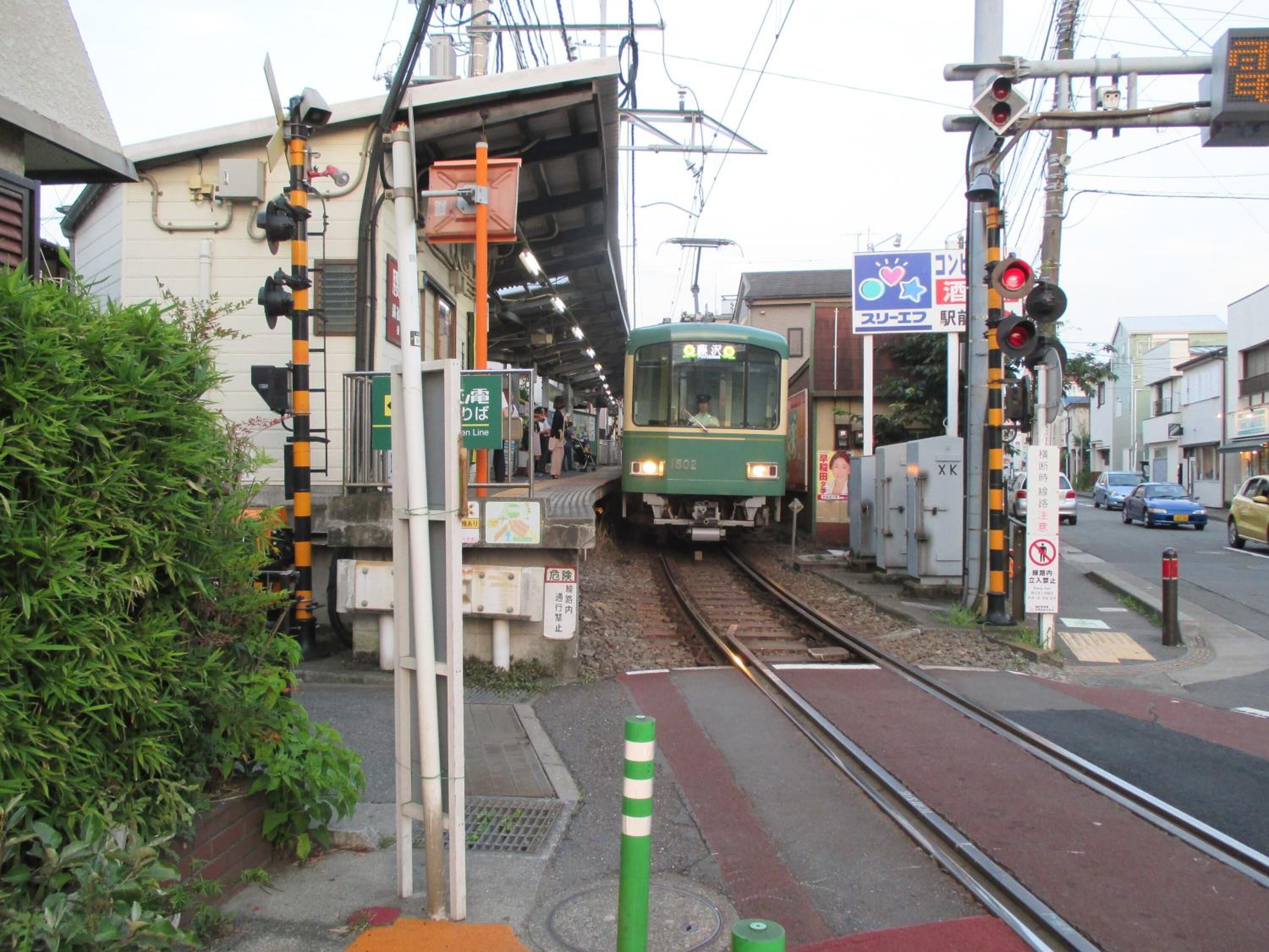 A train station platform with a green train approaching.