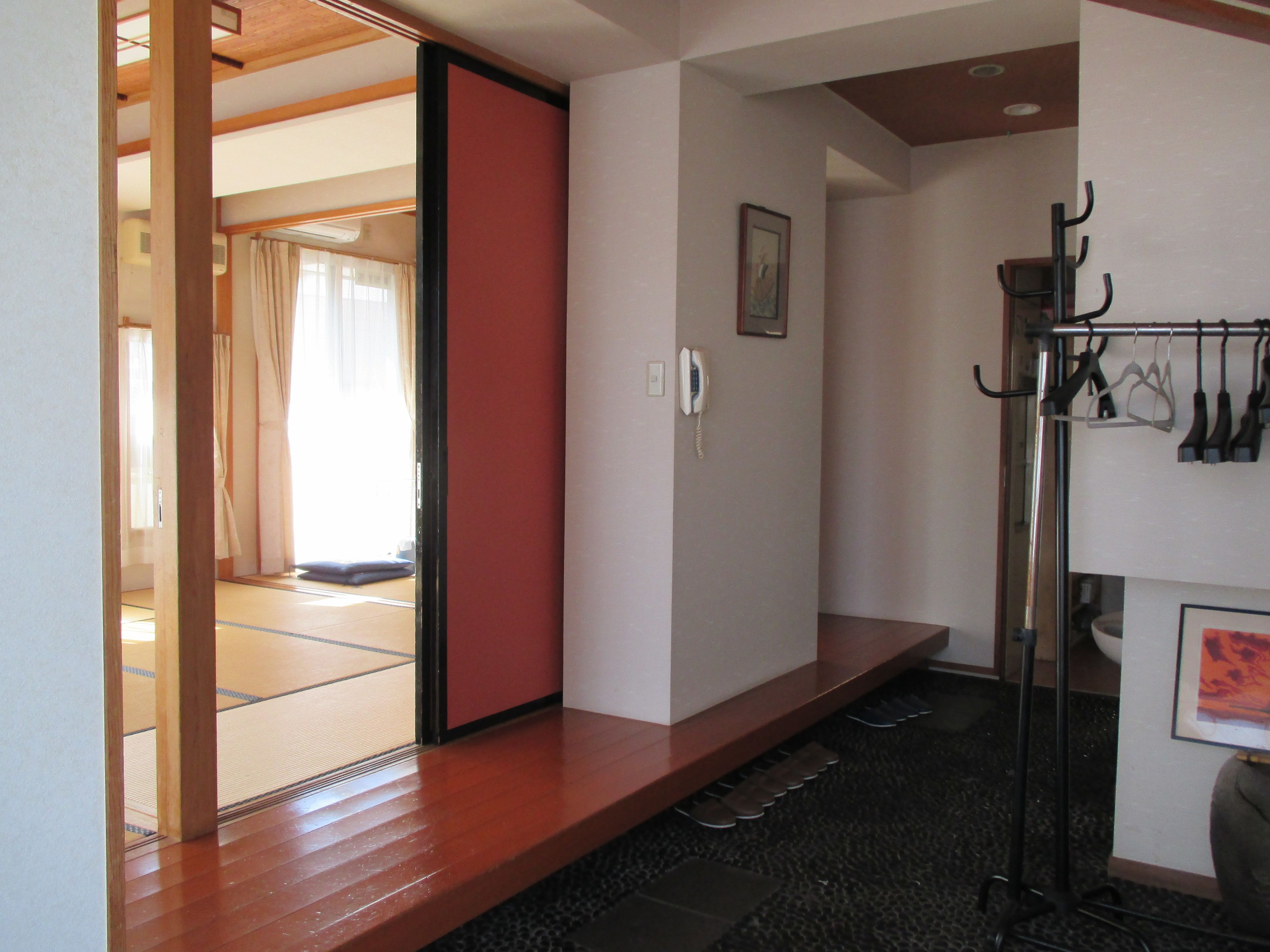 A room with tatami mat flooring, a wooden sliding door, a telephone, and a shoe rack.