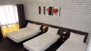 Habitación de hotel con tres camas individuales, pared con diseño de ladrillo y ventana con cortinas.