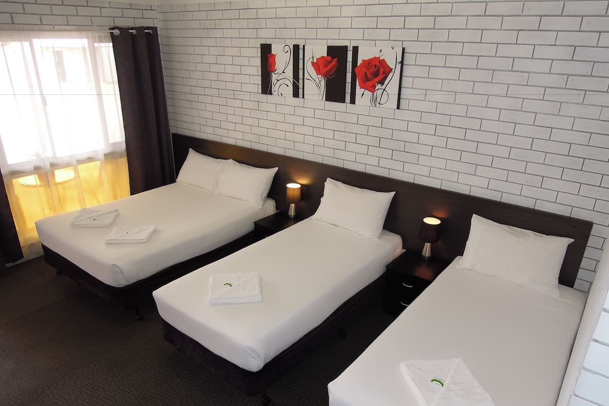 A hotel room with three single beds, a brick-patterned wall, and a window with curtains.