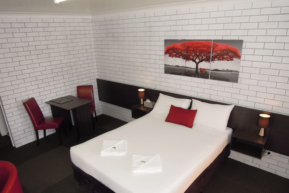 A hotel room with a bed, a desk, a chair, and a nightstand with a lamp.