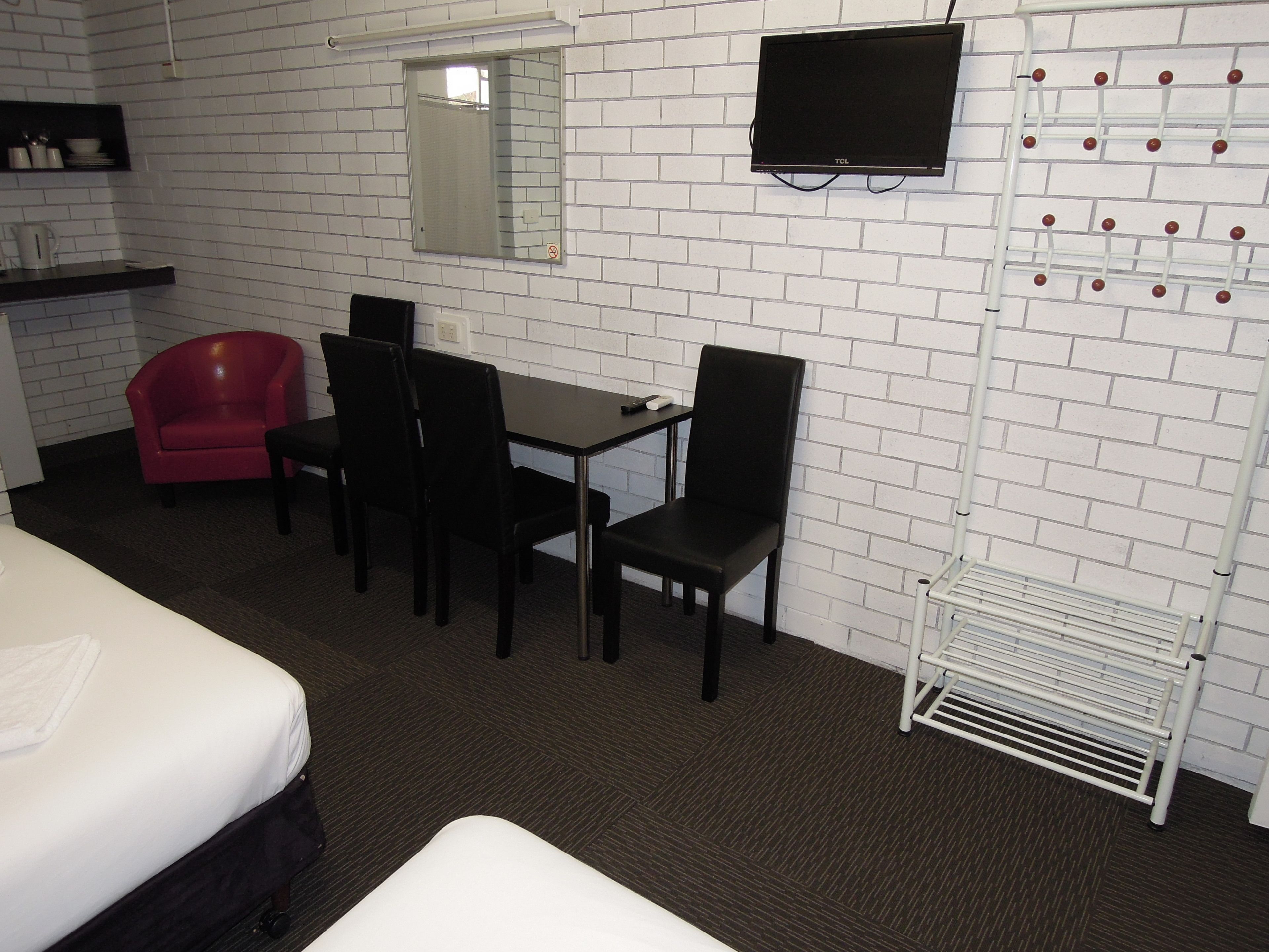 A hotel room with a bed, a desk with chairs, a TV, a mirror, and a white brick wall.