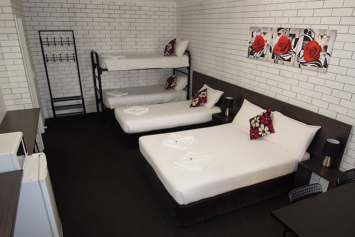 A hotel room with two single beds, a bunk bed, a desk, a chair, a small table, a lamp, and a wall art piece.