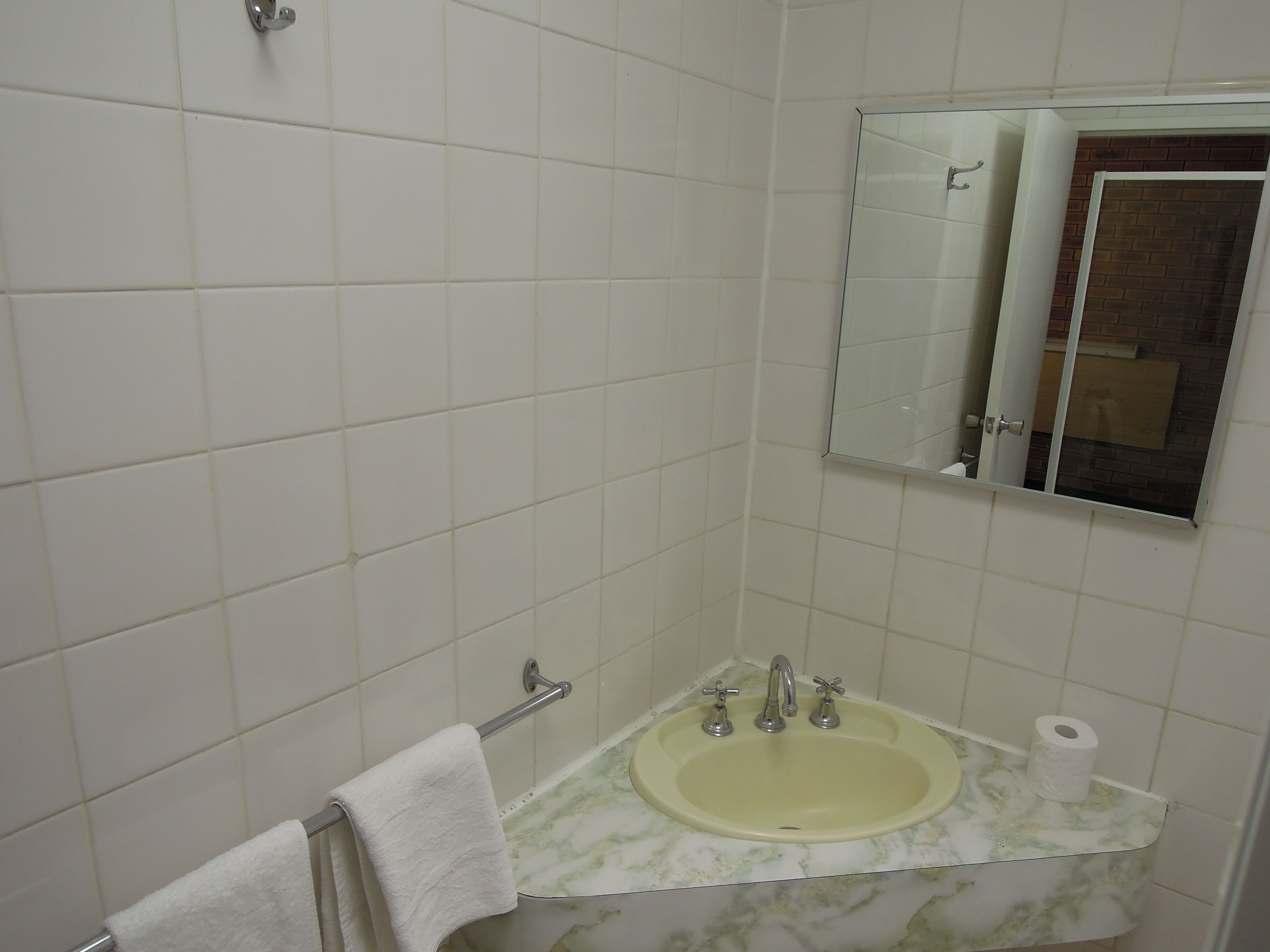 Un baño con azulejos blancos, un lavamanos con encimera de mármol, un perchero y un espejo.
