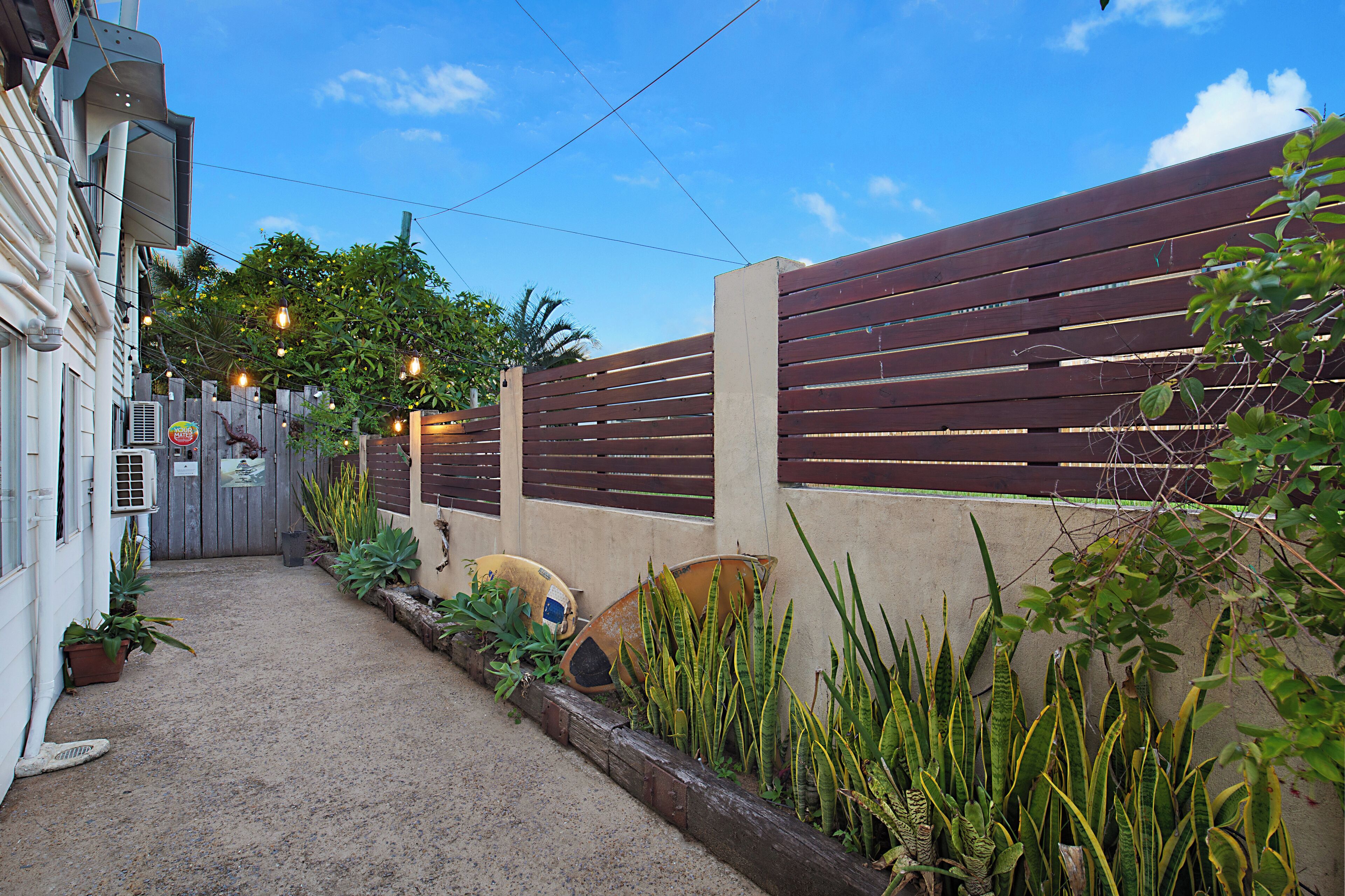A narrow pathway leading to a gated entrance with a wooden fence and a concrete wall.