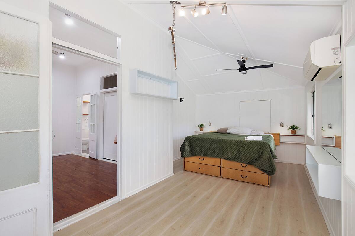 A bedroom with a bed, bedside tables, a ceiling fan, and an air conditioning unit.