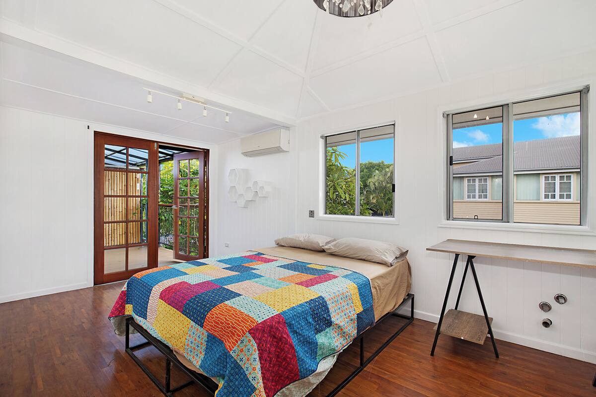 A bedroom with a large bed, a window with a view of buildings, and a wooden floor.