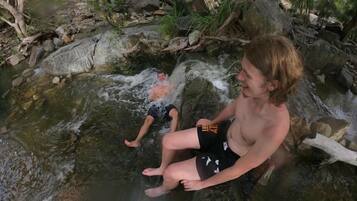 A person sitting on a rock by a flowing stream in a forested area.
