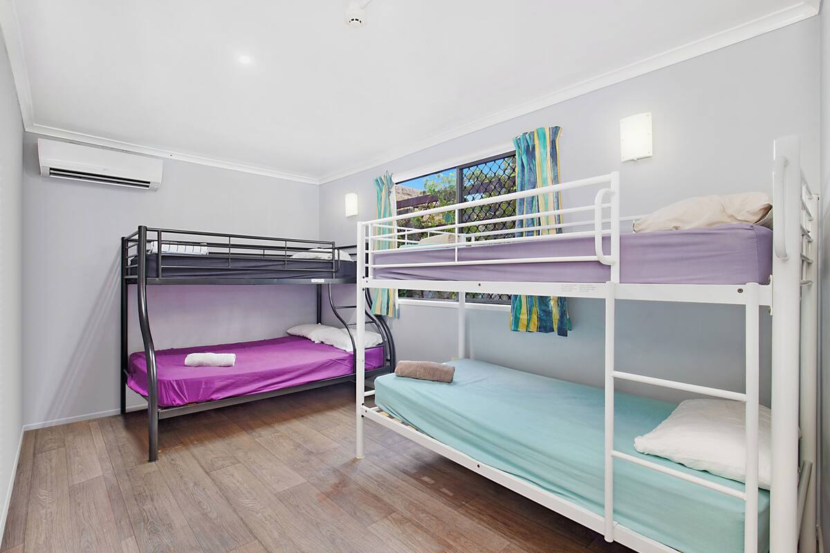 A room with two bunk beds, wooden flooring, and a window with curtains.