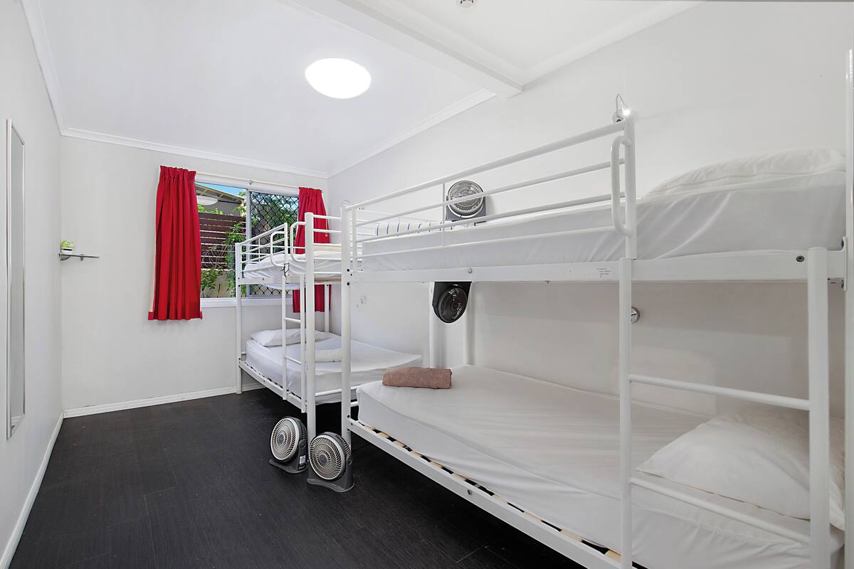 A bunk bed room with a window, red curtains, and two fans.