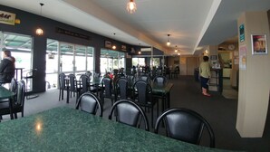 A restaurant interior with tables and chairs, a fire exit sign, and a clock on the wall.