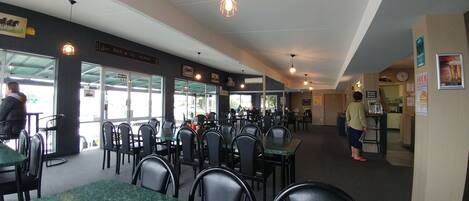 L’intérieur d’un restaurant, avec des tables et des chaises, un panneau indiquant la sortie de secours et une horloge au mur.