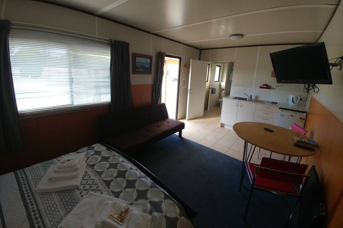 Quarto com cama, sofá, pequena mesa, televisão e cozinha compacta.