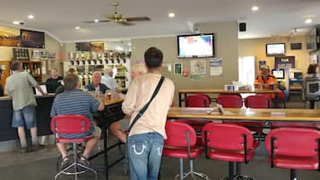 A bar area with red chairs, a counter with a bartender, and a television screen on the wall.