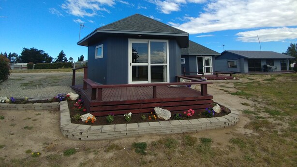A single-story building with a dark blue exterior, a wooden deck, and a small garden area with colorful flowers.