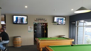 A pool hall with two pool tables, a wooden barrel, and two televisions mounted on the wall.