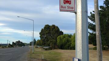 Placa de ponto de ônibus em um poste, com estrada e árvores ao fundo.