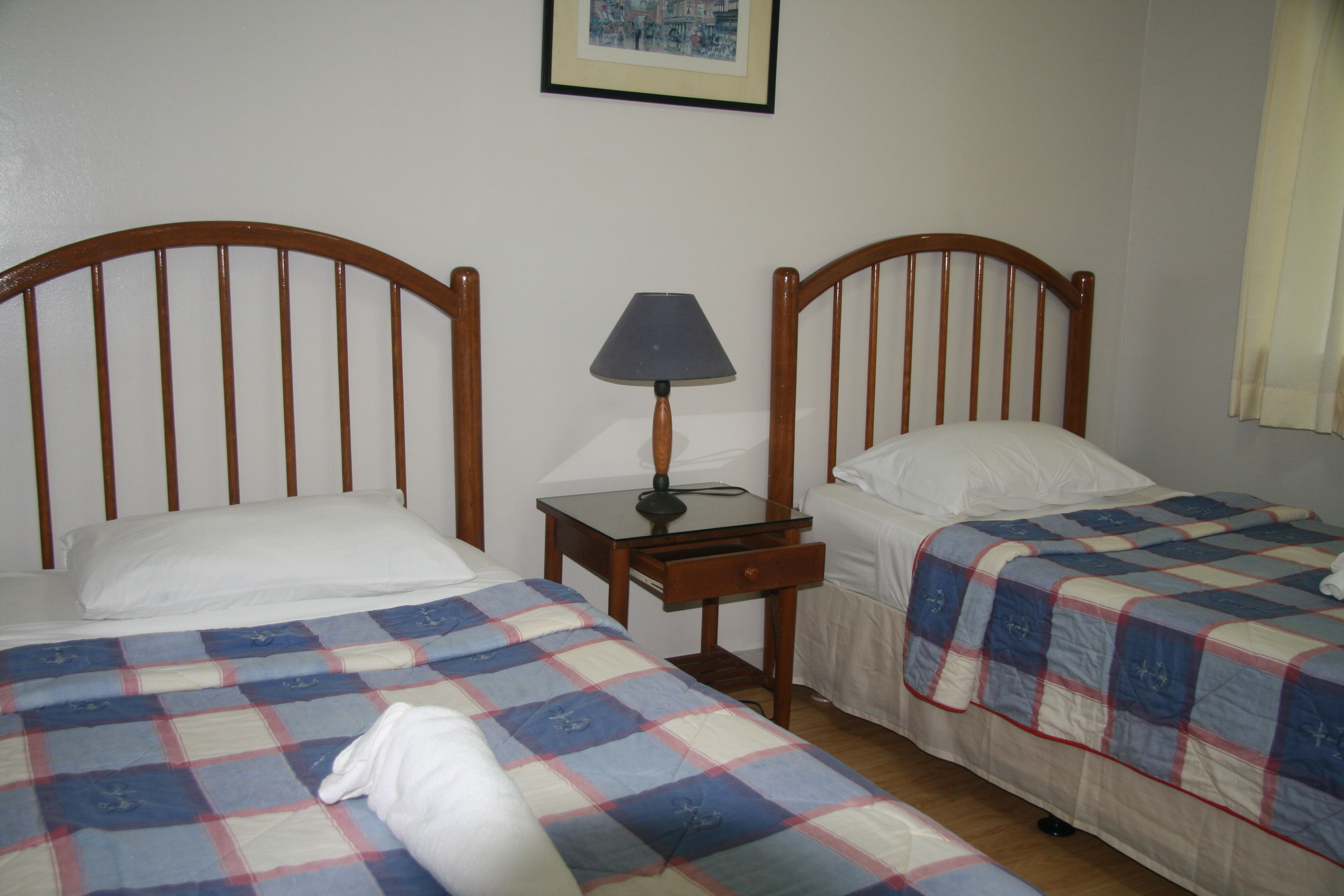 A bedroom with two single beds, a nightstand with a lamp, and a framed picture on the wall.