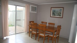 A dining area with a table and chairs, a sliding glass door, a window with an air conditioner, and a framed picture on the wall. - Vacation Villas at Subic Homes (Morong)