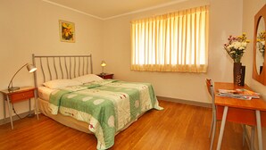 A bedroom with a bed, bedside tables, a desk, a chair, a window with curtains, and a vase with flowers. - Vacation Villas at Subic Homes (Morong)