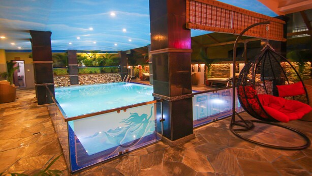 A swimming pool with glass panels, a hanging chair, and a stone-tiled floor. - Kuti Resort and Spa (Pokhara)