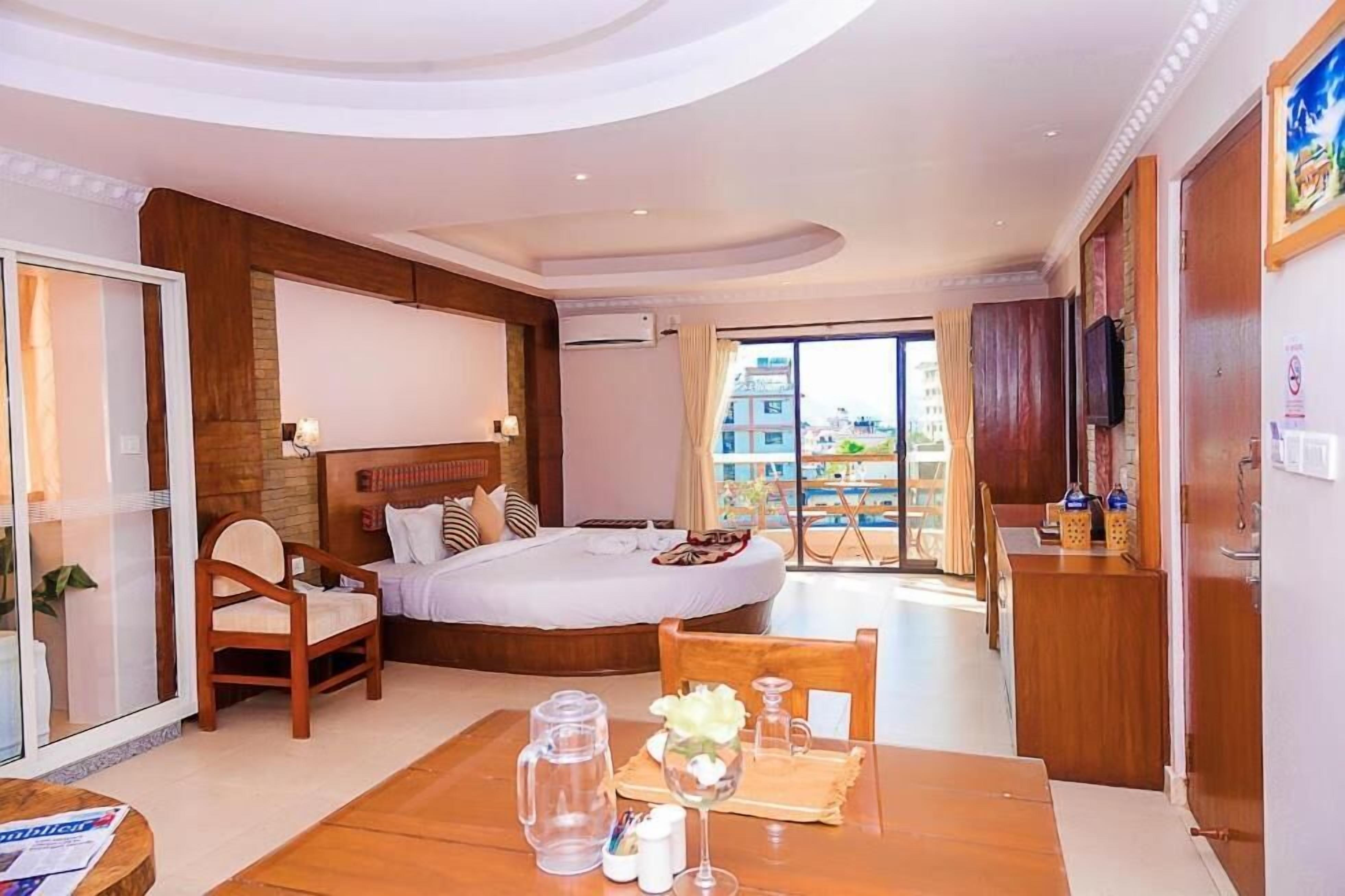 A hotel room with a bed, a dining table with a pitcher and glasses, a chair, a TV, and a view of the city.