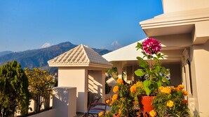A building with a tiled roof, a small structure with a sloped roof, and a potted plant with flowers. - Kuti Resort and Spa (Pokhara)