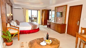 A hotel room with a bed, a dining table with a bottle and glasses, a potted plant, and a TV on the wall. - Kuti Resort and Spa (Pokhara)