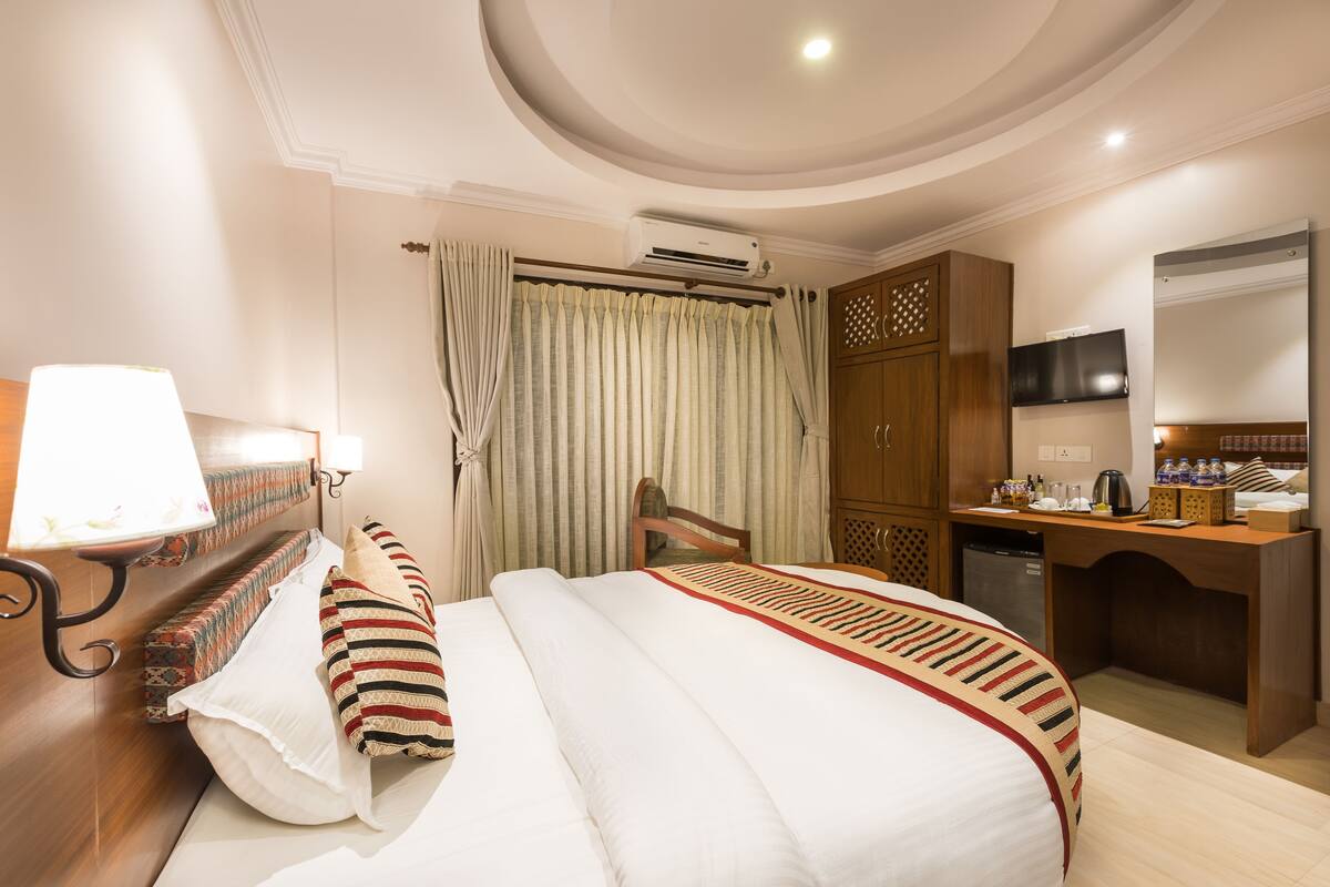 A hotel room with a bed, a desk, a television, and an air conditioning unit.