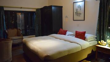 Une chambre d’hôtel avec un grand lit, une chaise, un bureau avec une lampe et une fenêtre avec des rideaux.