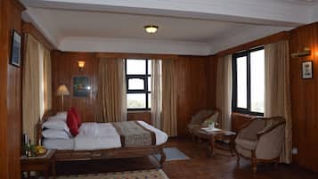Quarto de hotel com uma cama grande, uma cadeira, uma mesa pequena e uma janela.
