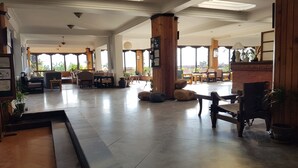 A spacious lobby with a mix of seating areas, including sofas and chairs, and a central column. There are potted plants and a tiled floor. - The Fort Resort (Baluwapati Deupur)