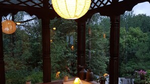 A covered outdoor seating area with wooden furniture and a hanging light fixture. - The Fort Resort (Baluwapati Deupur)