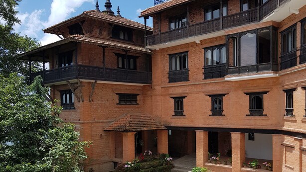 A courtyard with a traditional building featuring multiple balconies and a central seating area. - The Fort Resort (Baluwapati Deupur)