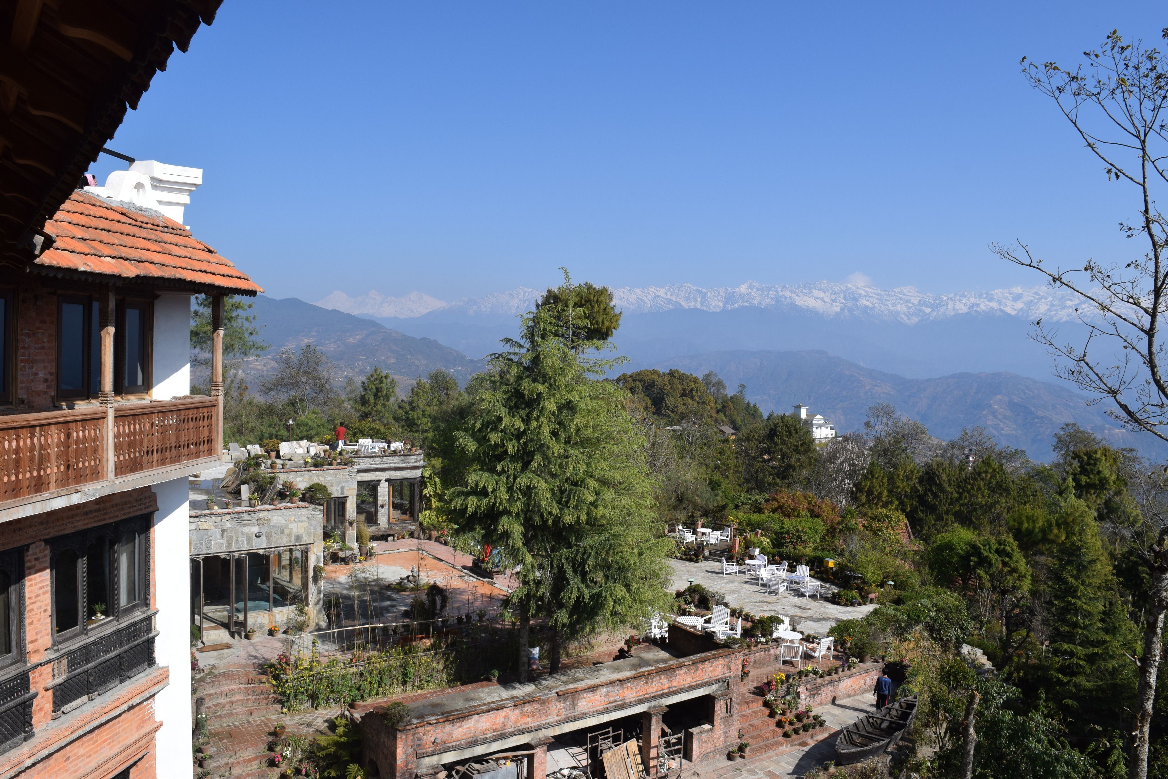 A traditional building with a red-tiled roof, a balcony, and a view of snow-capped mountains in the background.