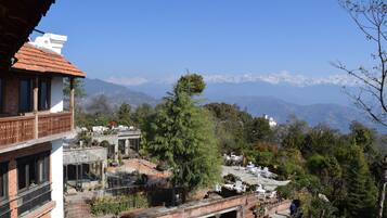 A traditional building with a red-tiled roof, a balcony, and a view of snow-capped mountains in the background.
