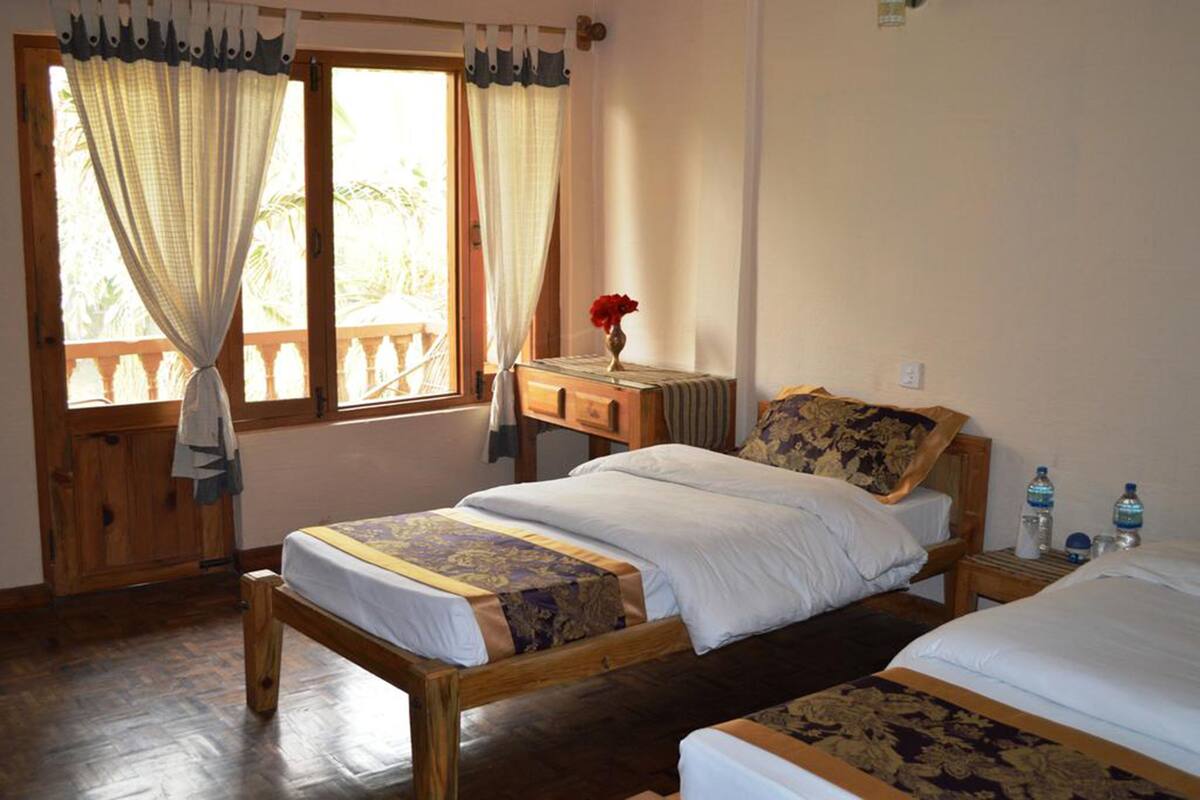 A room with two wooden beds, a small table with a vase of flowers, and a window with curtains.