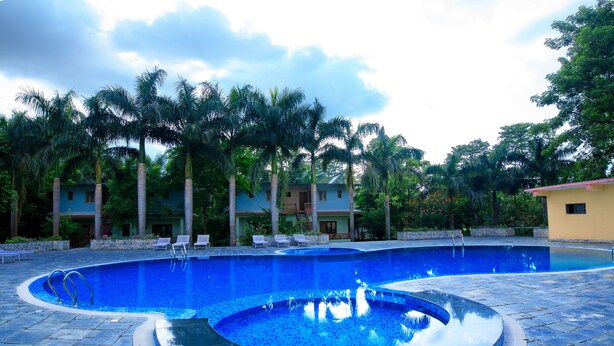 A swimming pool with a circular hot tub, surrounded by lounge chairs and palm trees. - Chitwan Paradise Hotel (Sauraha)