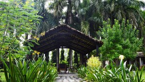 A stone pathway leading to a thatched-roof pavilion surrounded by lush greenery and tall palm trees. - Chitwan Paradise Hotel (Sauraha)