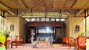 A room with a bamboo ceiling, wooden chairs, and a central statue. - Chitwan Paradise Hotel (Sauraha)