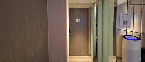 Un pasillo moderno con piso de madera, una pared divisoria de vidrio y un altavoz blanco con luz azul.