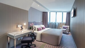 Een hotelkamer met een bed, bureau, stoel en een groot raam.