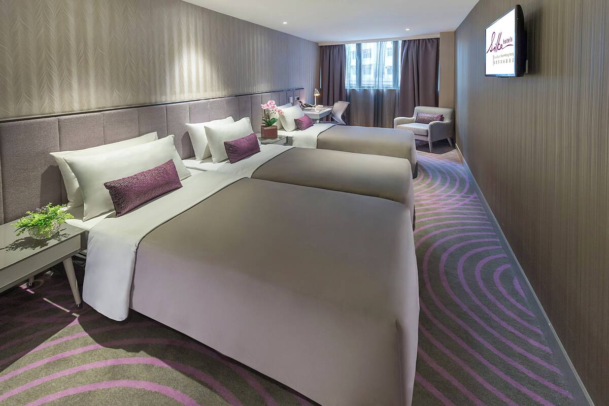 Ein Hotelzimmer mit einem großen Bett, einem Schreibtisch, einem Sessel und einem Fernseher an der Wand.