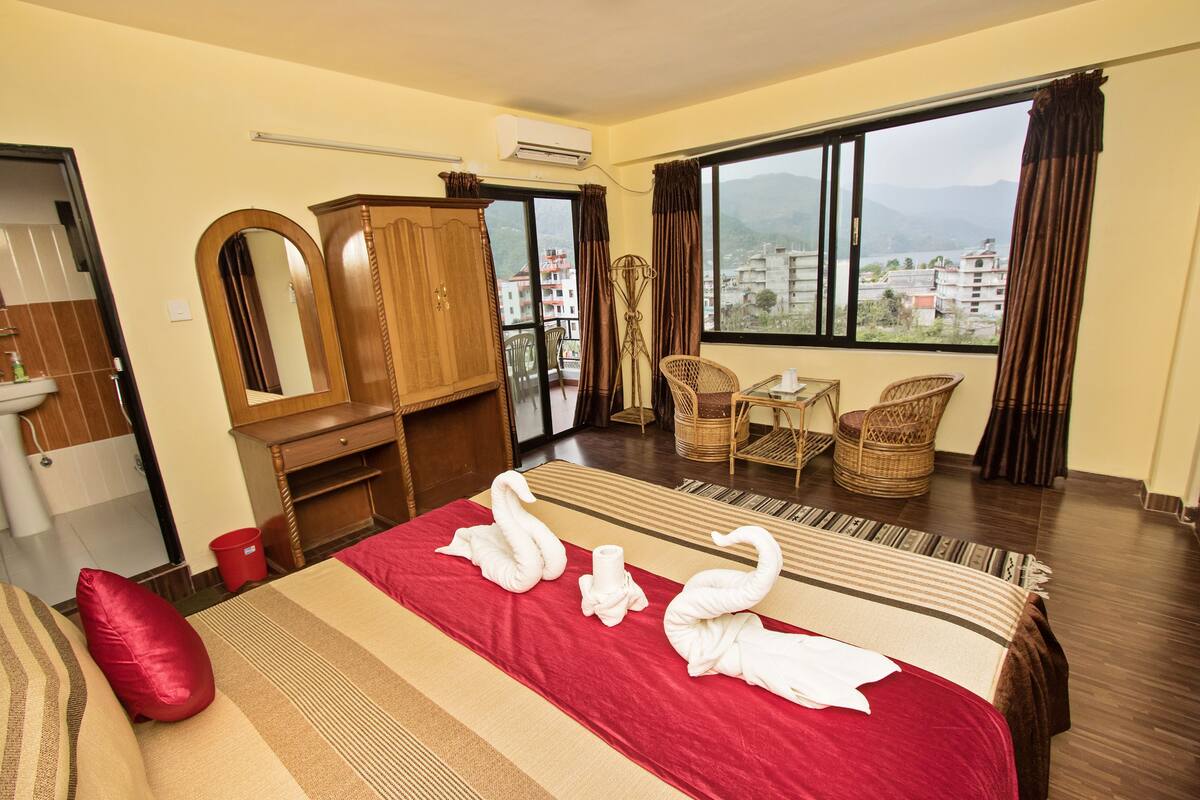 A hotel room with a bed, a wardrobe, a desk, a chair, a window with a view, and a balcony.