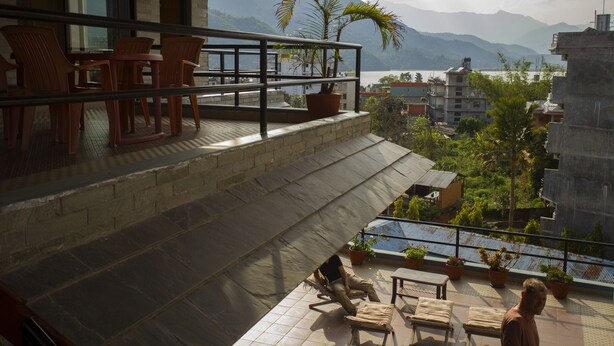 Un balcón con mobiliario exterior, plantas en macetas y vistas a las montañas y al agua.