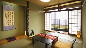 A traditional Japanese room with tatami flooring, a low table, a cushioned bench, a sliding door with shoji screens, and a hanging scroll with calligraphy. - Resort Ryokan Yadokari (Echizen)