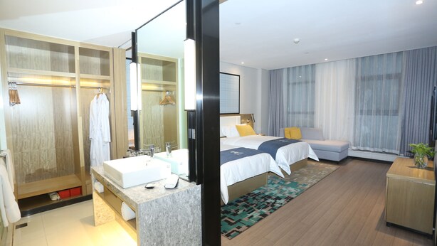 A modern hotel room with a large bed, two bedside tables, a bathroom with a sink and mirror, and a walk-in closet. - ECHARM Hotel Zhengzhou High Tech Zone (Zhengzhou)